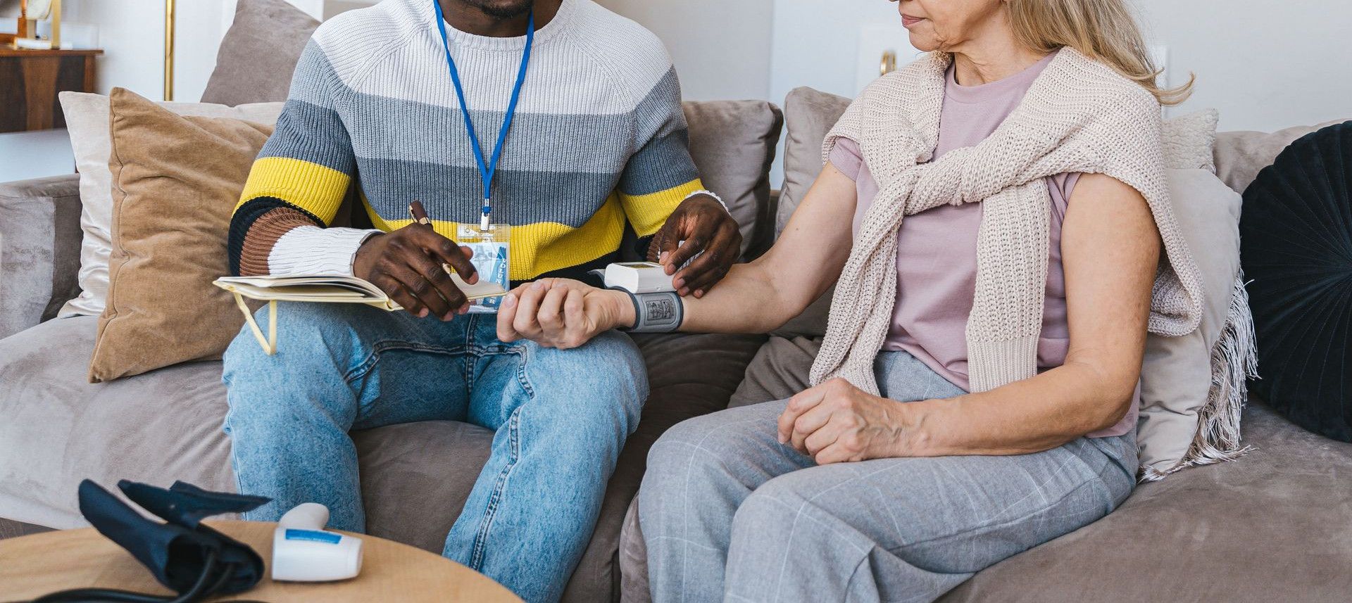 Volunteer checking elderly woman's blood pressure at home. Compassionate healthcare support.